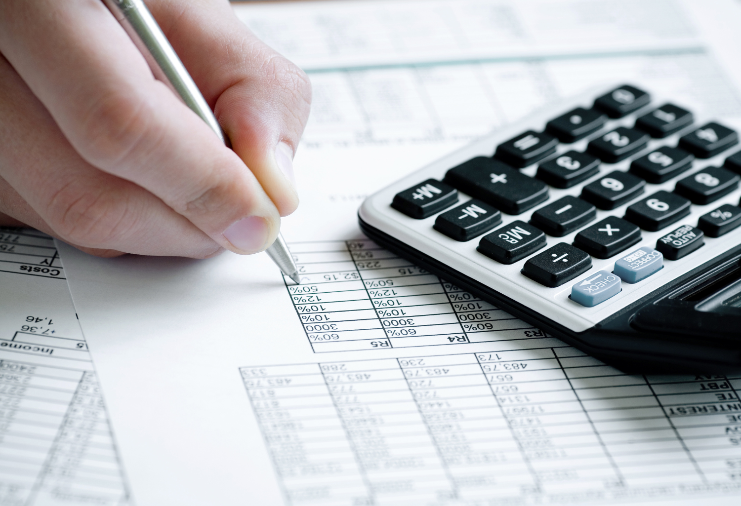 Person writing on paper next to a calculator.